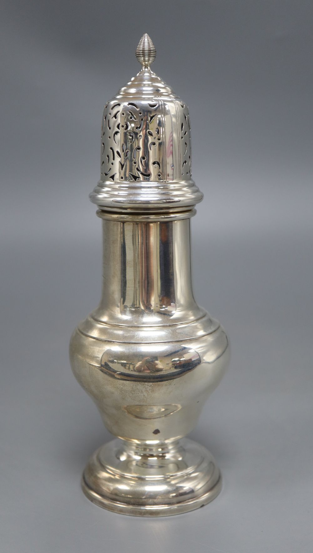 A silver vase shape sugar shaker, with pierced domed cover, ribbed finial on circular base, Birmingham 1932, 7.6oz., height 23cm